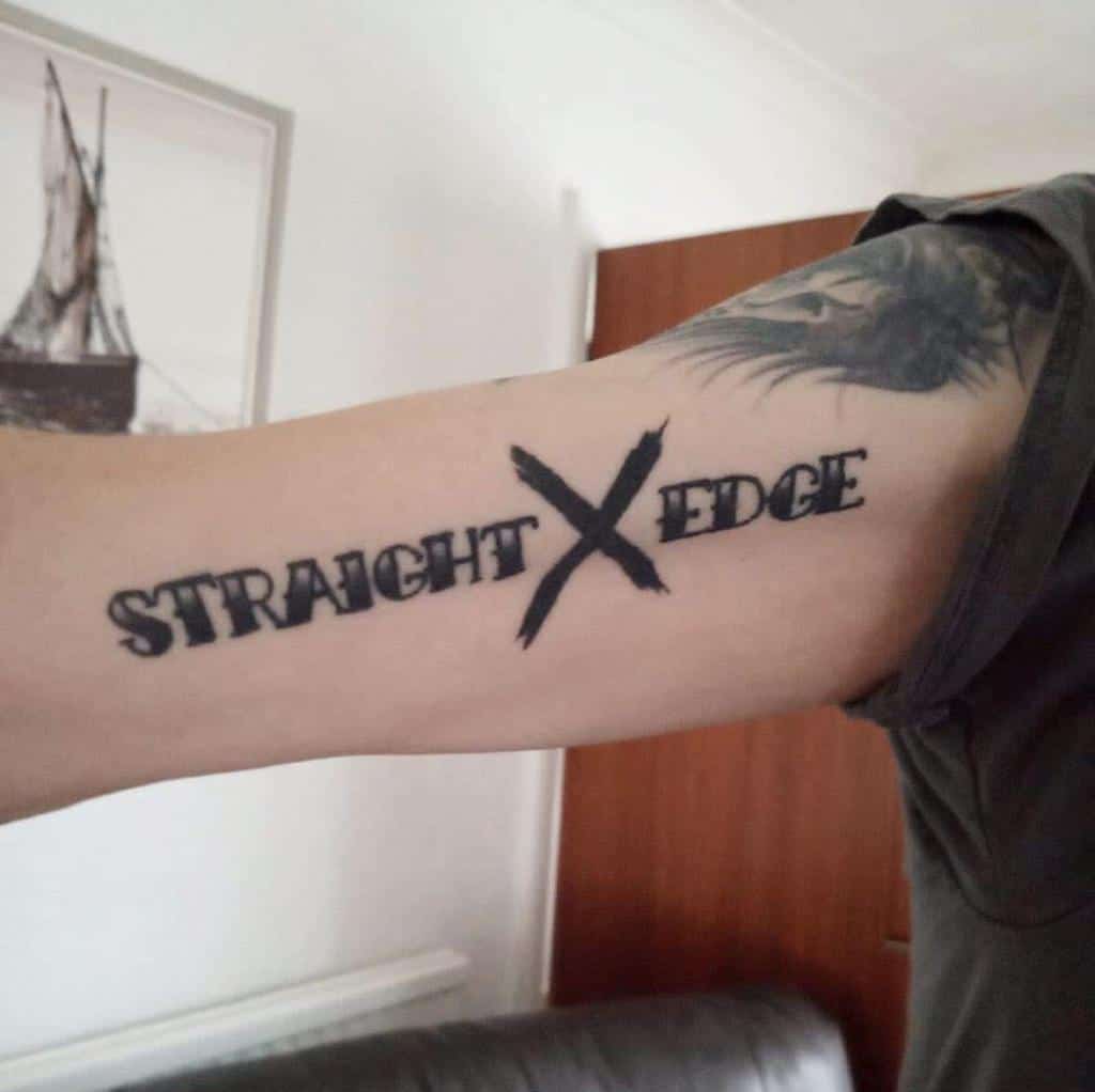 Straight edge tattoo on the inner arm with bold distressed lettering and a large brushstroke 'X' symbolizing a clean lifestyle