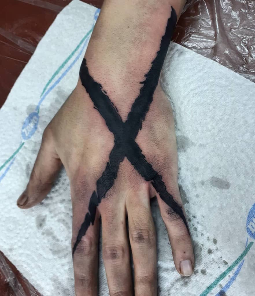 A hand with a large black X straight edge tattoo covering the entire back