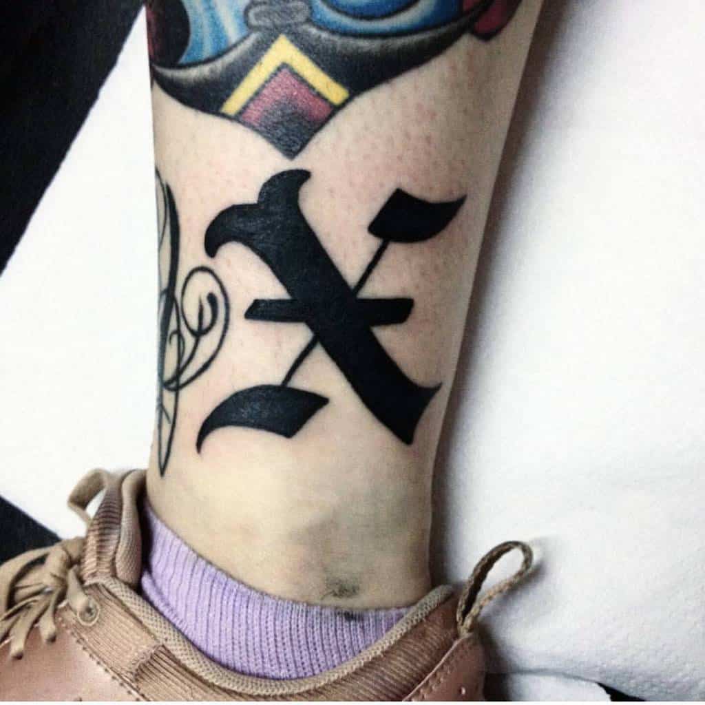 A large black straight edge tattoo of a bold, stylized "X" letter
