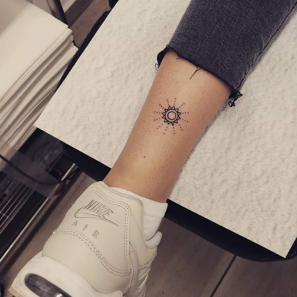 Minimalistic tattoo of a small sun with dotted rays, placed on the ankle for a simple and subtle design