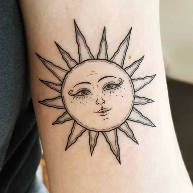 A tattoo of a stylized sun with a human face on someone's arm