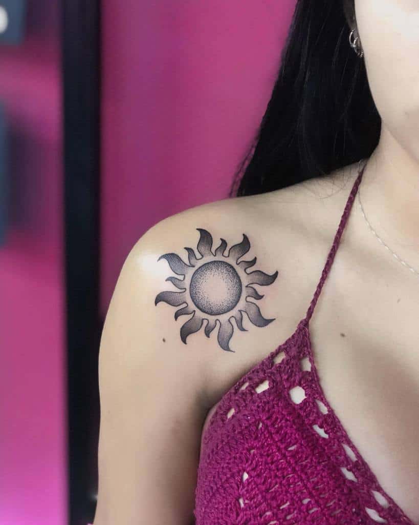 Black ink sun tattoo with dotwork shading in the center, placed on the shoulder with flame-like rays extending outward
