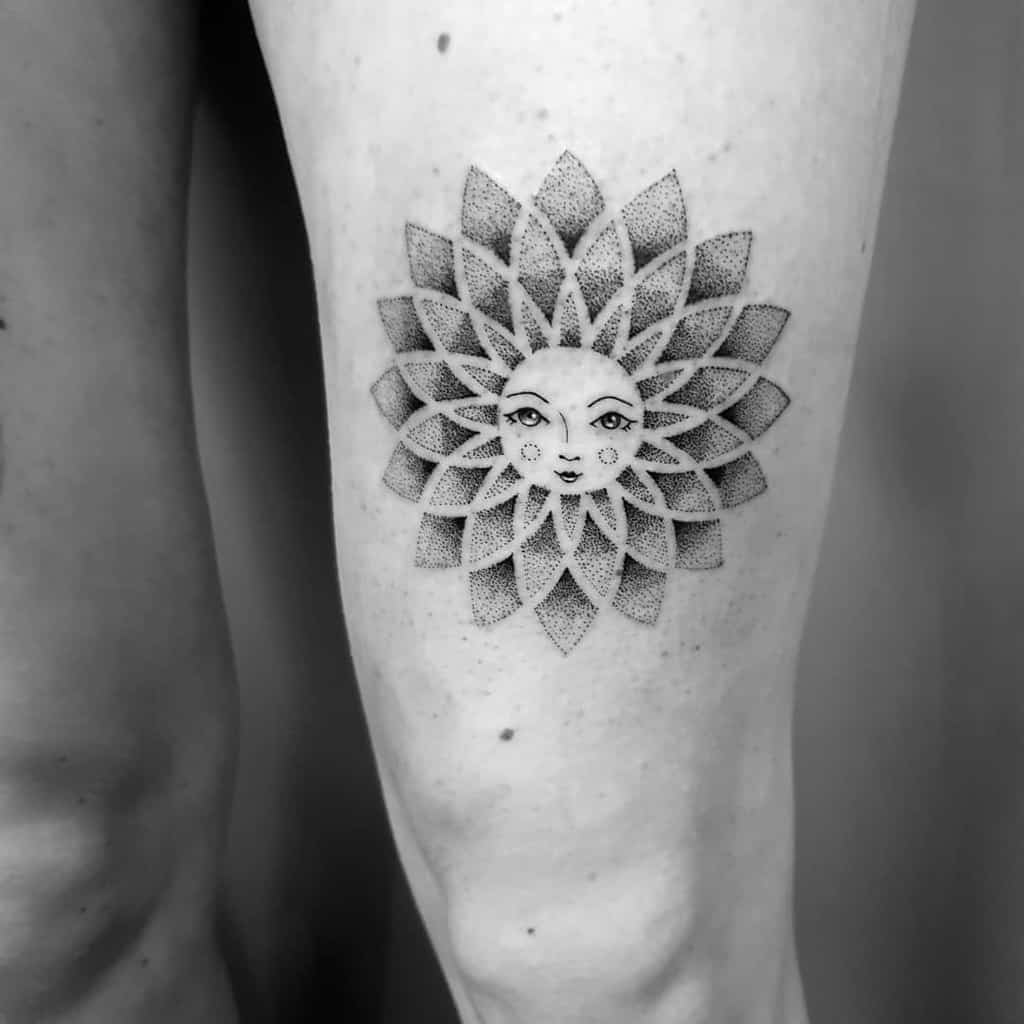 Tattoo of a sun with a face and petal-like rays on a person's thigh