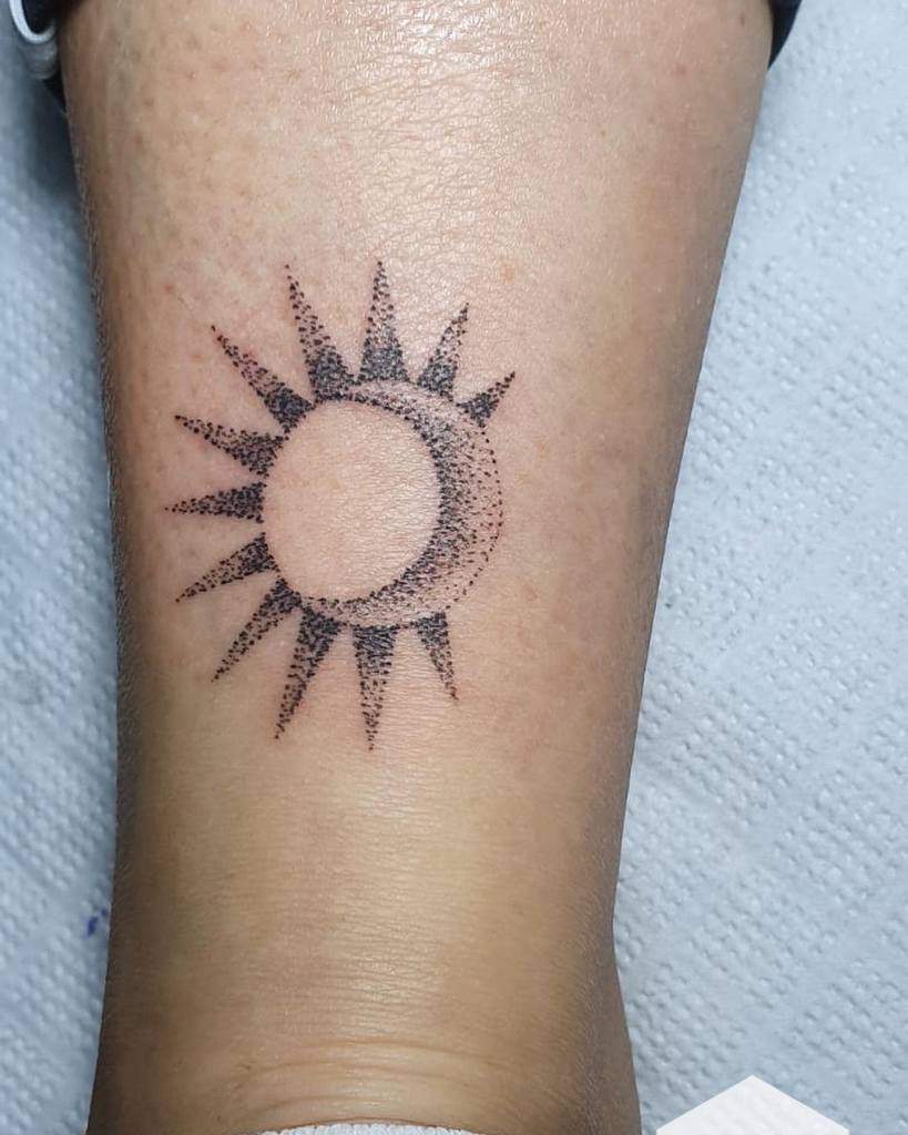 Tattoo of a sun with a crescent moon inside on a lower leg