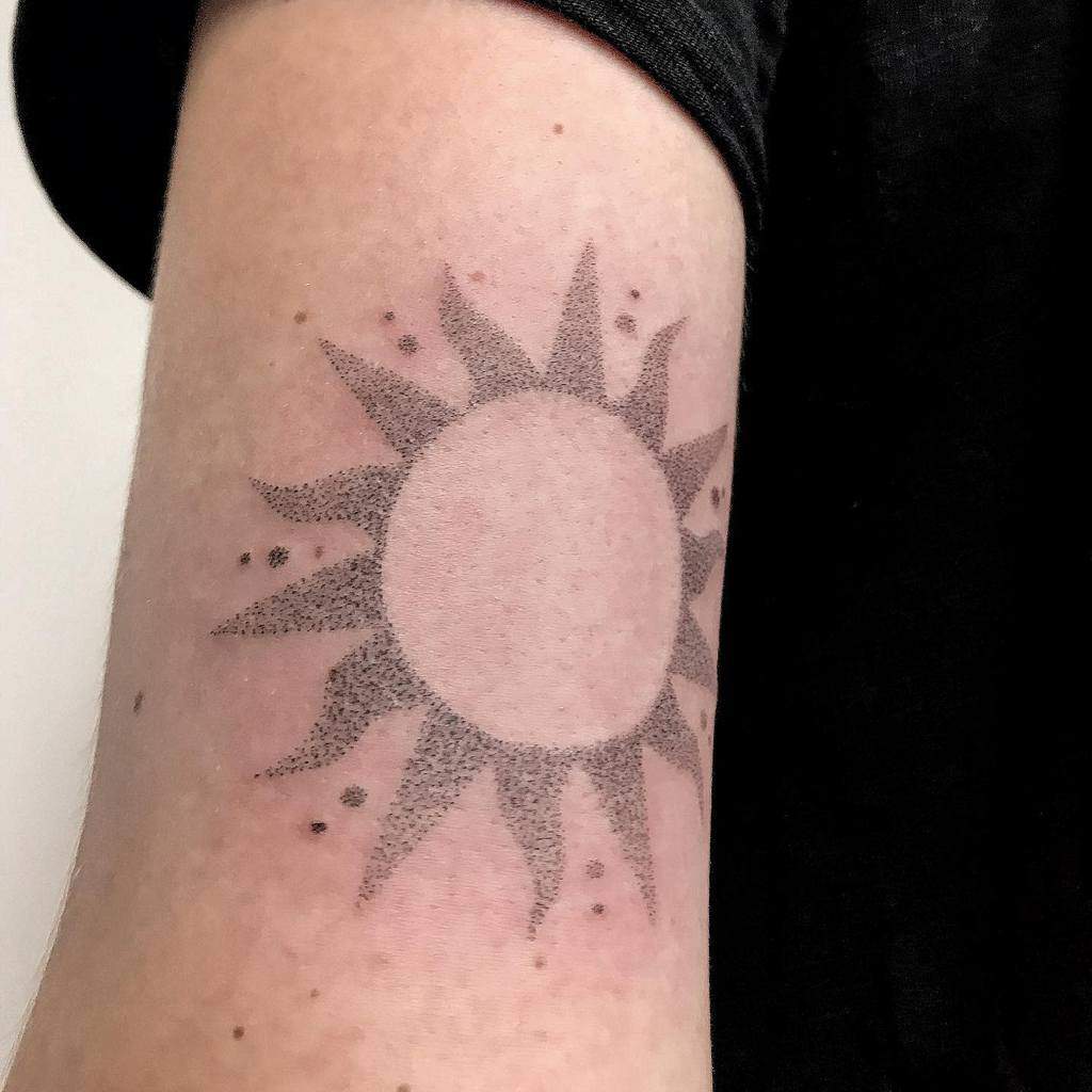 A black dotted sun tattoo with rays on a person's arm