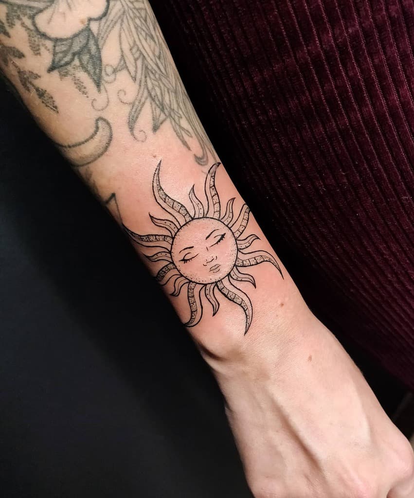 Forearm tattoo of a serene sun face with radiating rays
