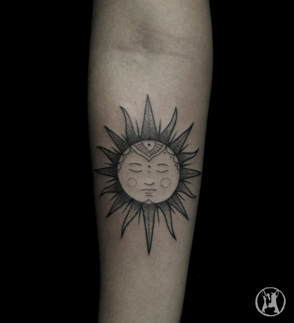 Forearm tattoo of a sun with a serene face, adorned with intricate dot and line designs