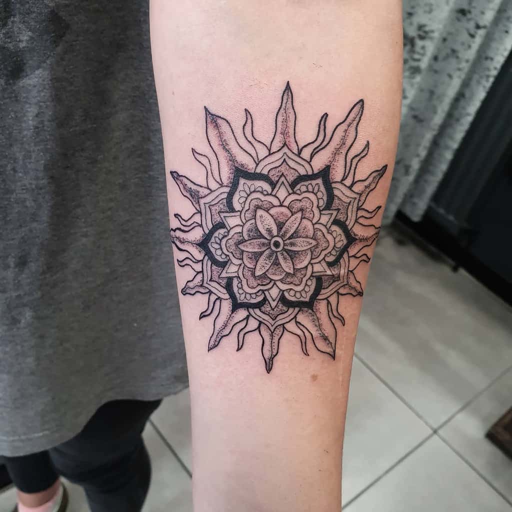 Intricate sun and mandala tattoo featuring detailed floral patterns at the center with radiant, flame-like rays