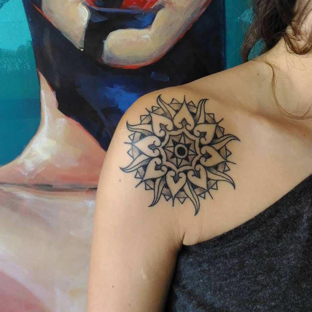 Ornate sun and mandala tattoo with symmetrical heart and star shapes, placed on the shoulder, featuring detailed linework