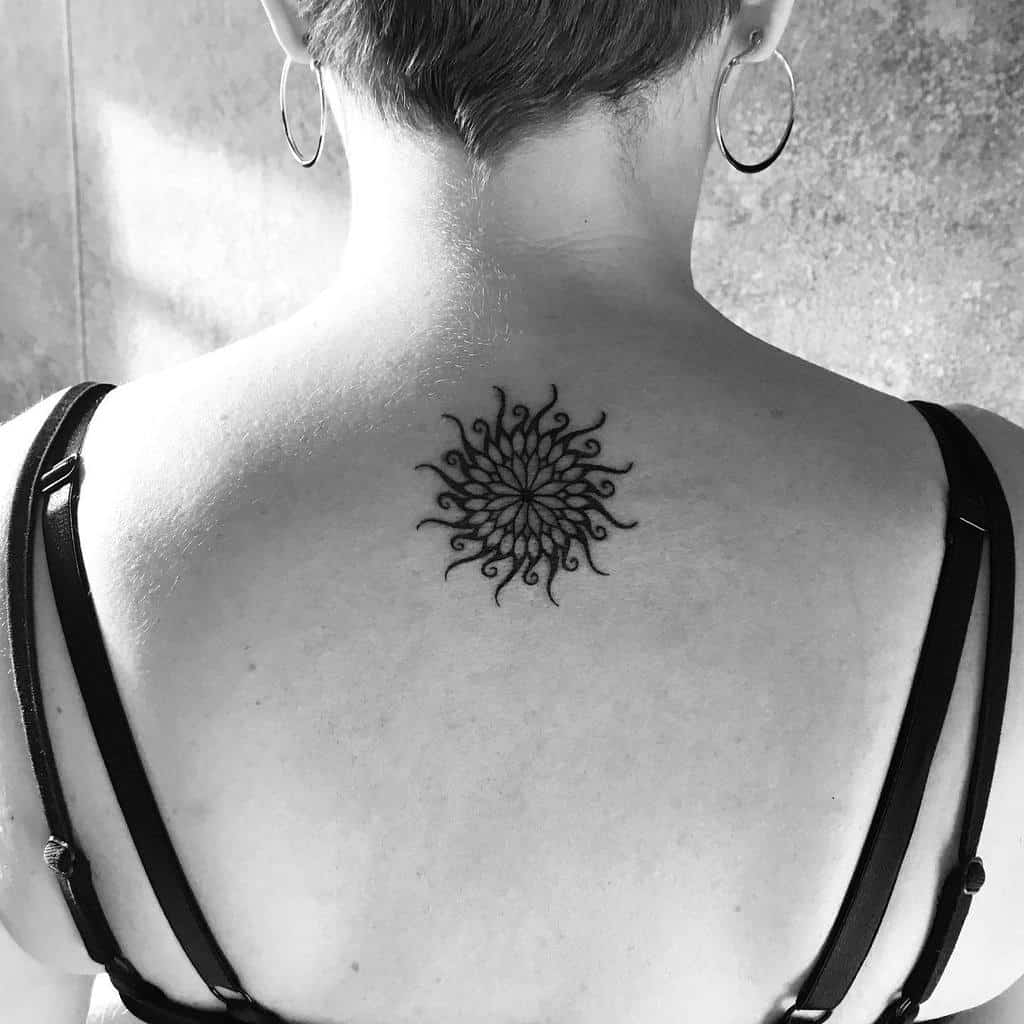 Intricate black ink sun and mandala tattoo featuring swirling rays and geometric details, placed on the upper back