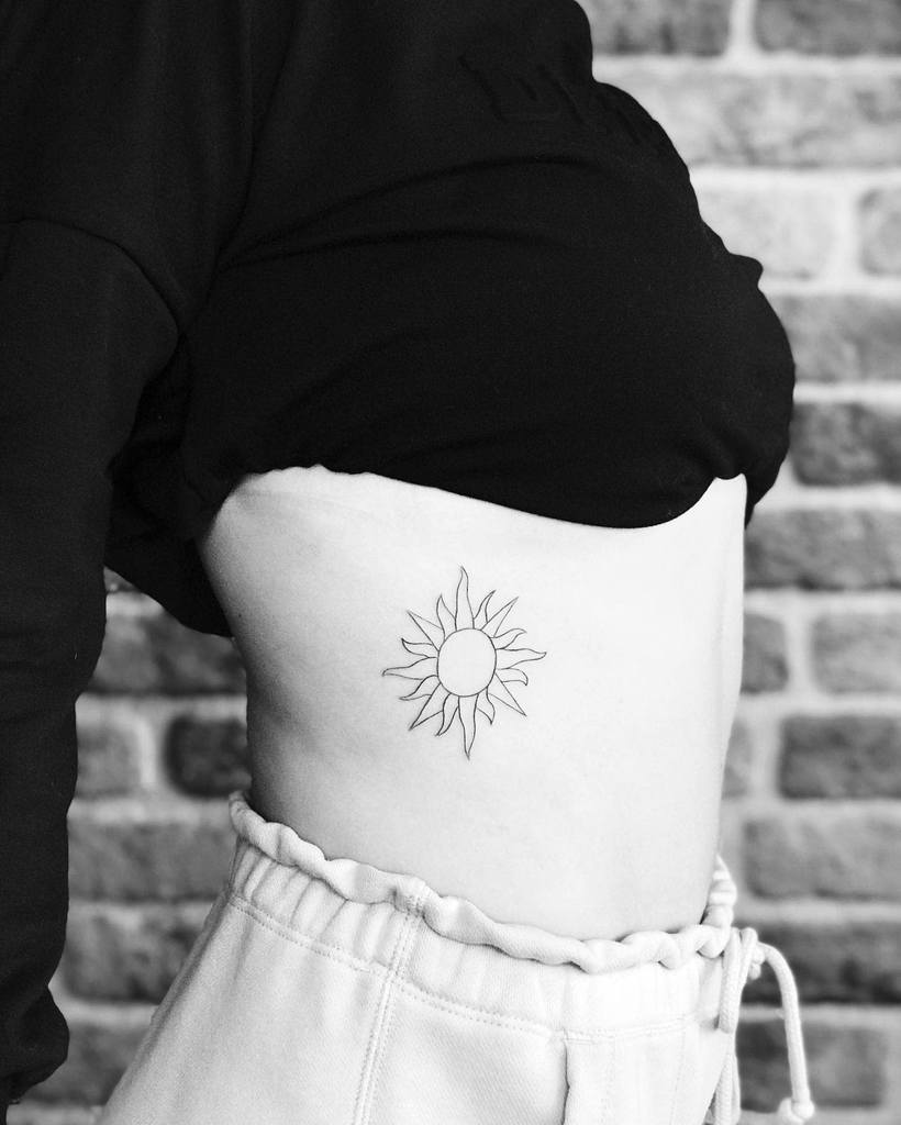 Minimalist black ink sun tattoo with thin rays, placed on the ribcage for a simple yet elegant design