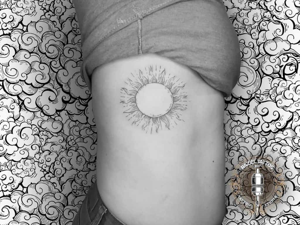 Black and white tattoo of a sun on a person's right side