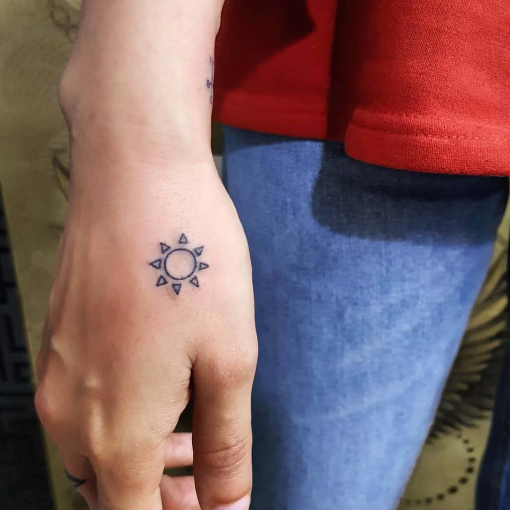 A small sun tattoo on the back of a person's hand