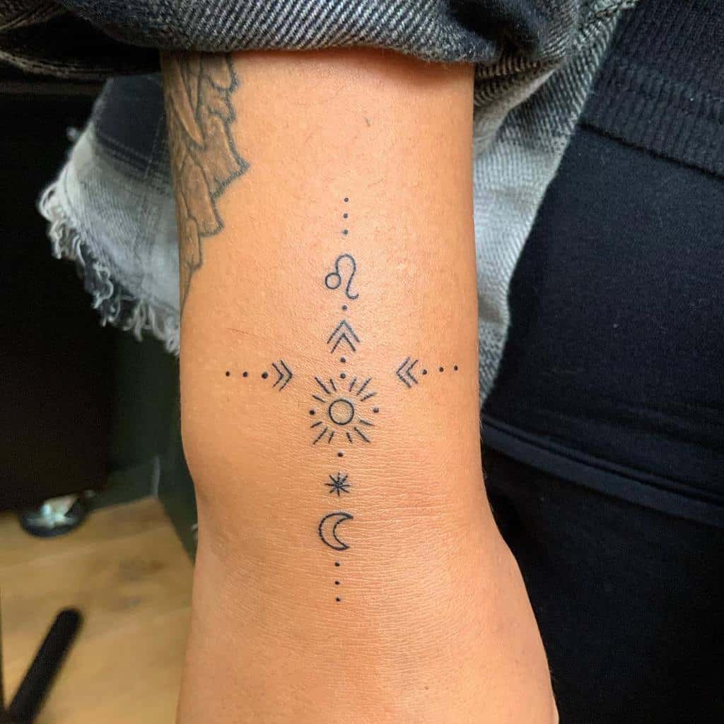 Forearm tattoo featuring a sun at the center with various symbols around it, including a crescent moon
