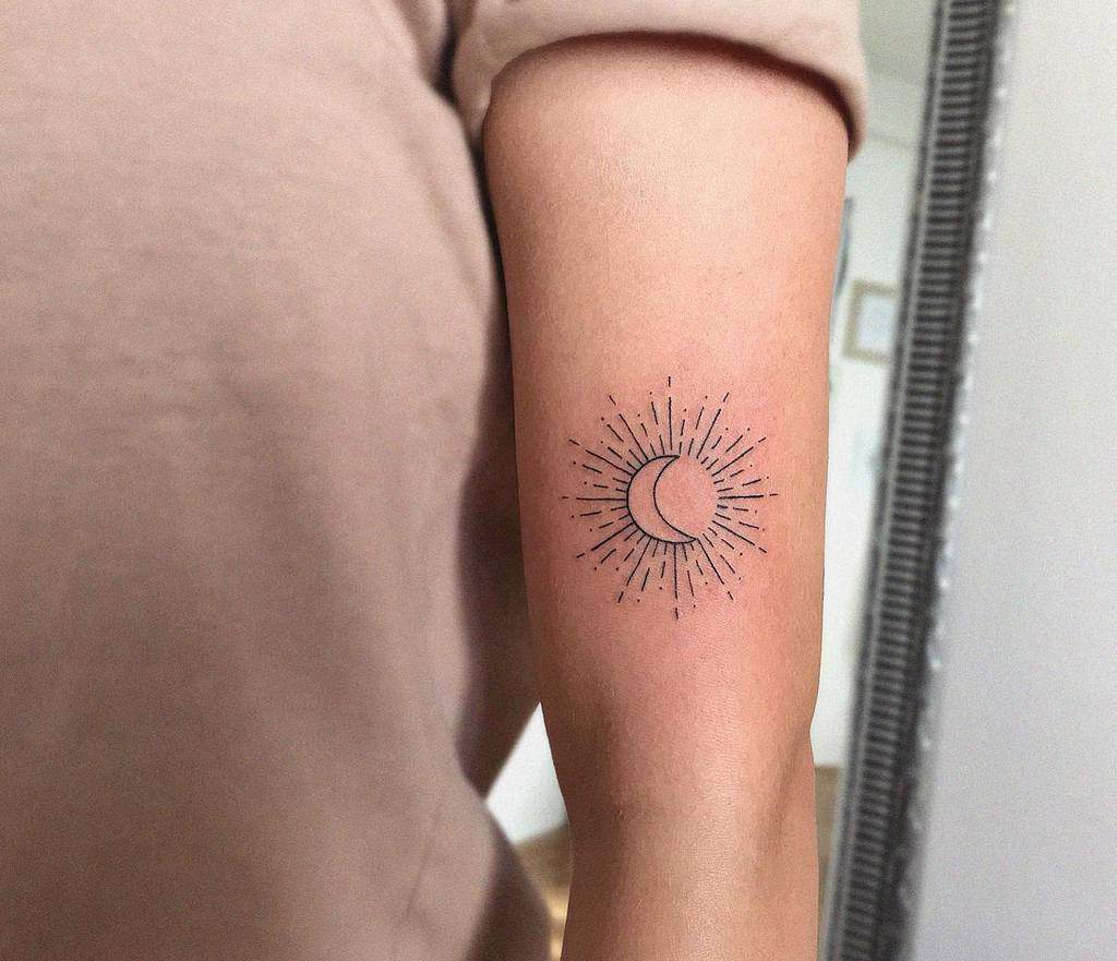 Minimalist sun and crescent moon tattoo with fine lines and dotted rays, placed on the upper arm for a celestial design
