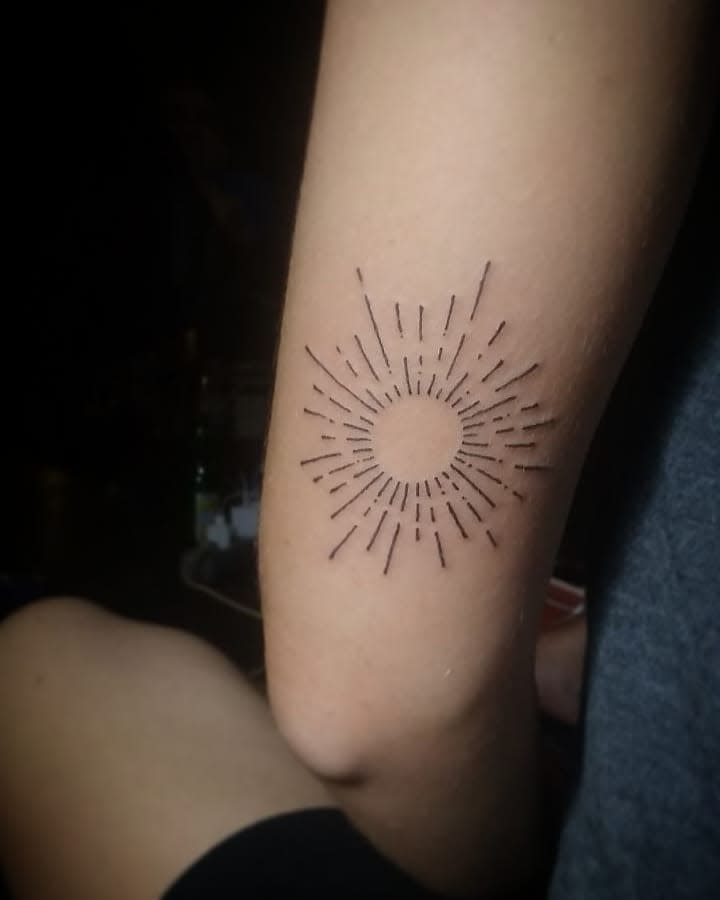 Minimalist sunburst tattoo on the back of an arm