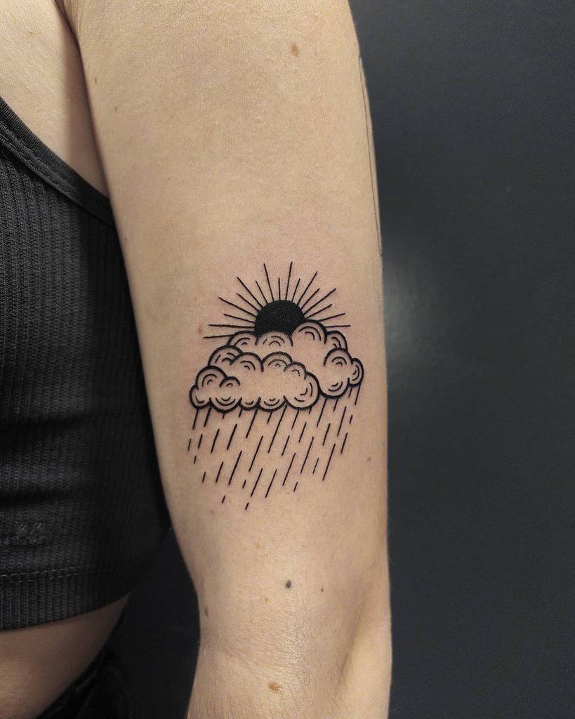 Black and white tattoo of a cloud with rain and a sun on a person's upper arm