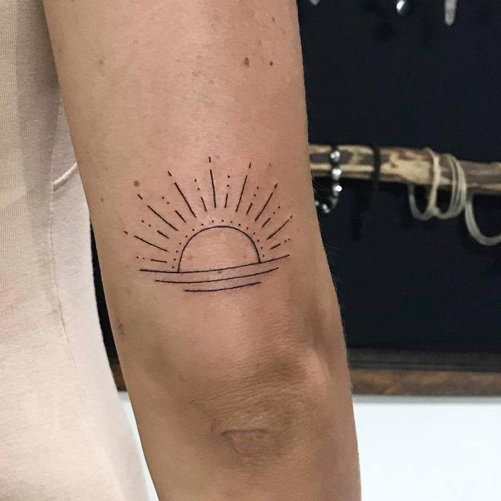Minimalist sunset tattoo with fine lines and dotted rays, placed on the upper arm, featuring a simple horizon design