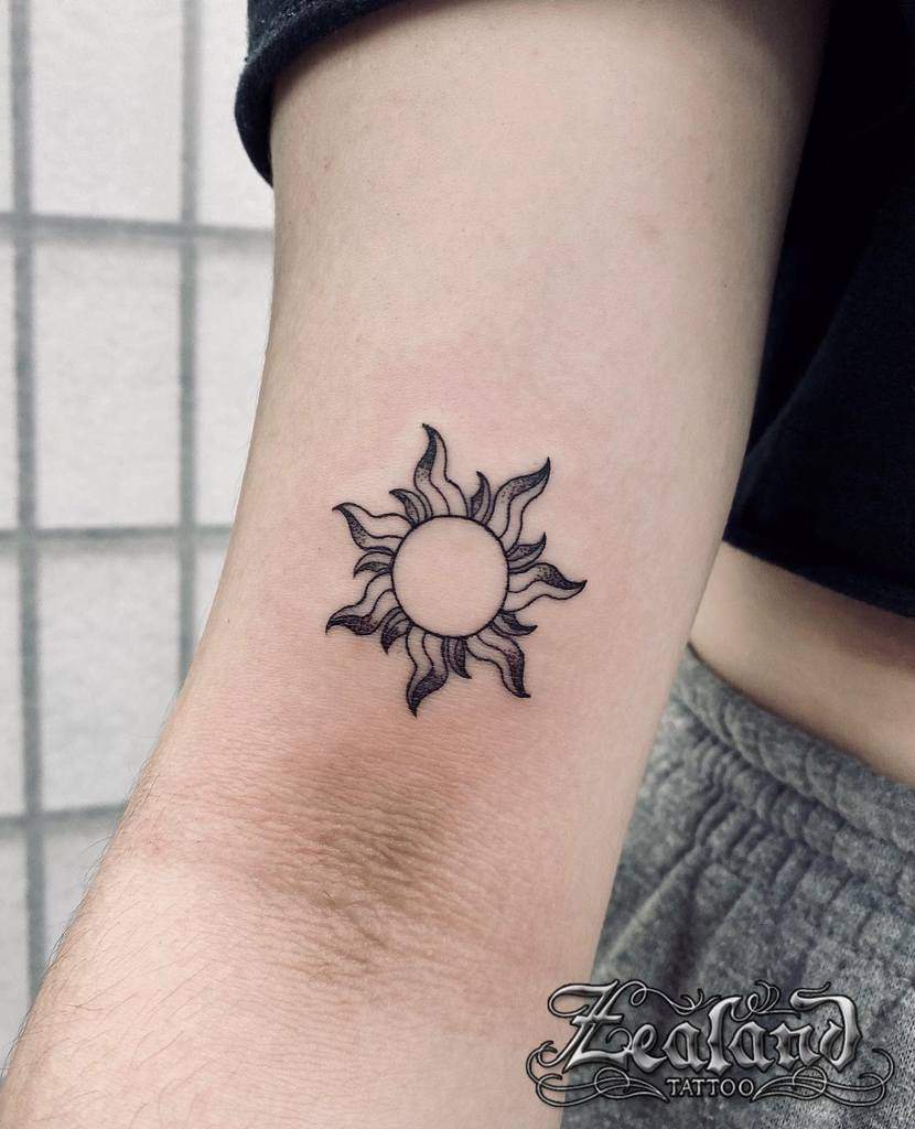 Tattoo of an outlined sun with wavy rays on an inner arm