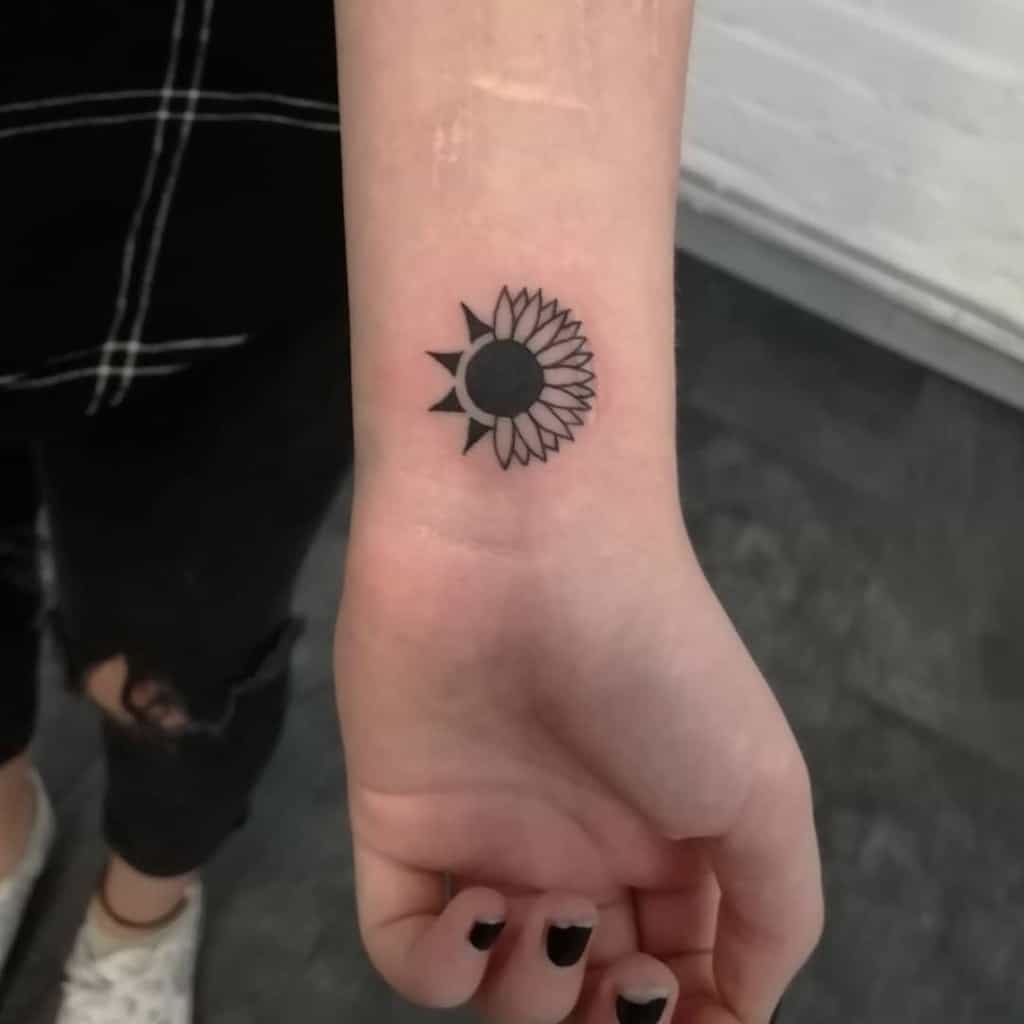 Wrist tattoo of a sunflower with the petals radiating from a solid black circle in the center