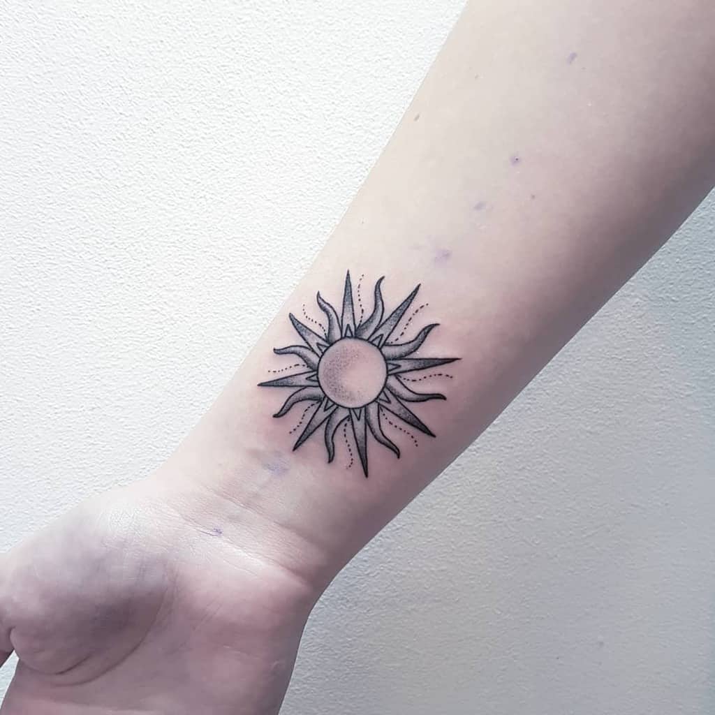 Black sun tattoo with detailed rays on the wrist