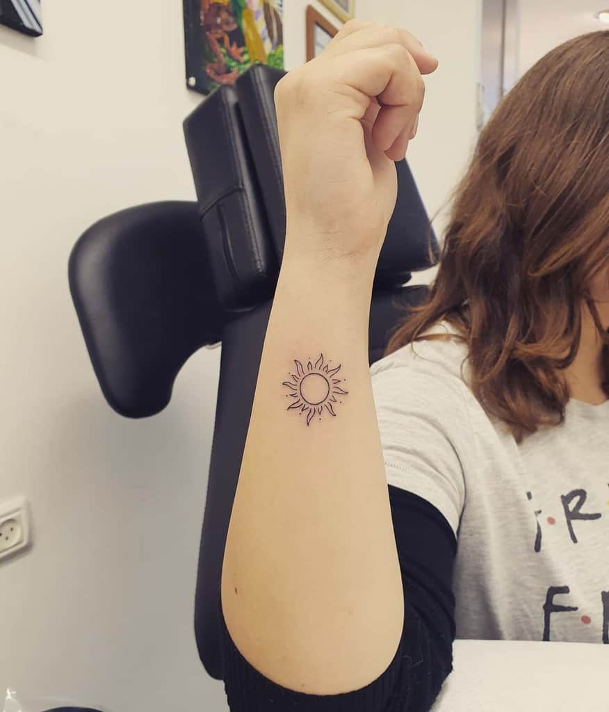 Small, minimalist sun tattoo with clean lines and wavy rays, placed on the inner forearm for a subtle and elegant look
