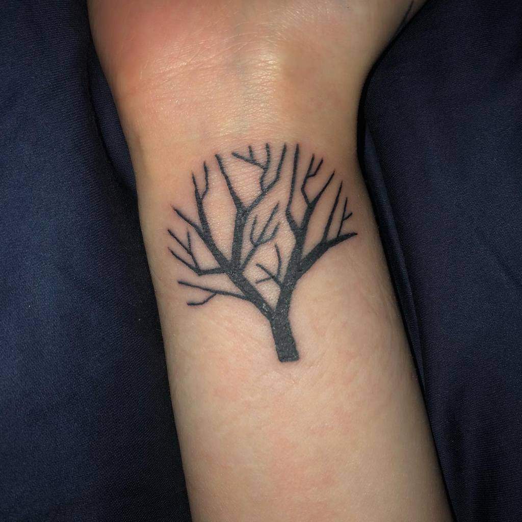 Tattoo of a leafless tree with branching limbs on the inside of a person's wrist