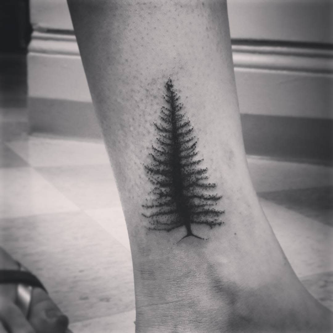Black and white tattoo of a pine tree silhouette on the ankle