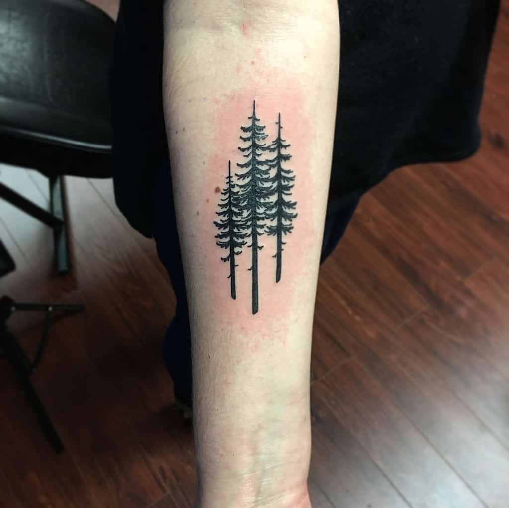 Tattoo of three tall pine tree silhouettes on an arm