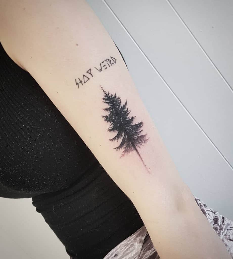 Tattoo of a tree silhouette and runic script on an upper arm