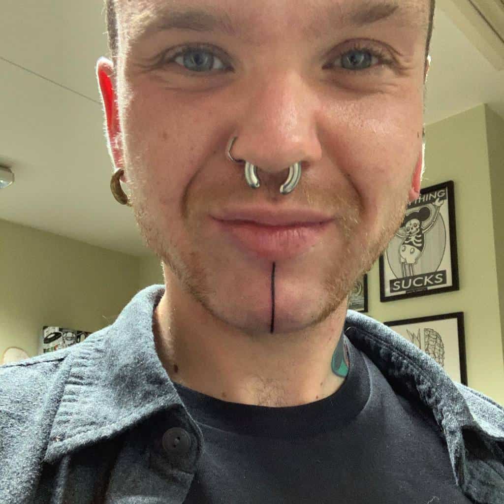 Man withlinear chin tattoo, and stretched ear lobes, smiling indoors