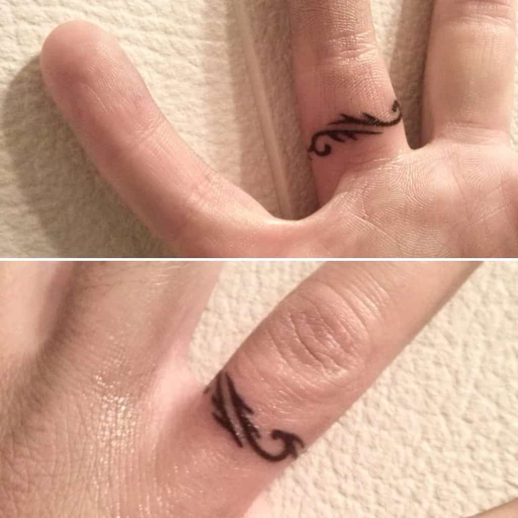 Close-up of two fingers with black, curved line ring tattoos resembling vines or waves on the sides