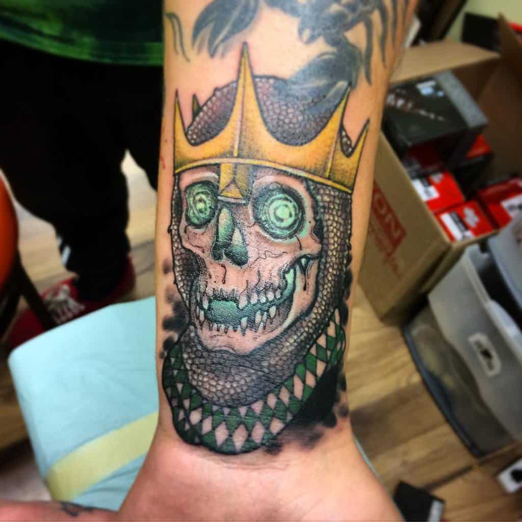 Colorful Dungeons & Dragons tattoo of a skeletal lich wearing a golden crown, glowing green eyes, and a serpent-like scaled collar