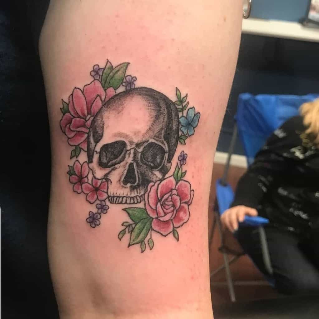 Tattoo of a skull with pink and purple flowers on an arm