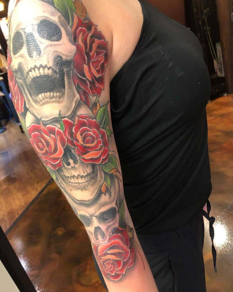 A vibrant tattoo featuring skulls and red roses covering a woman's arm