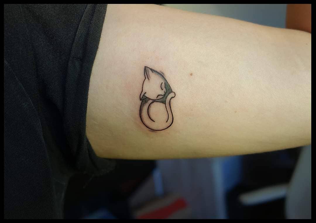 A minimalistic sleeping cat tattoo on the upper arm
