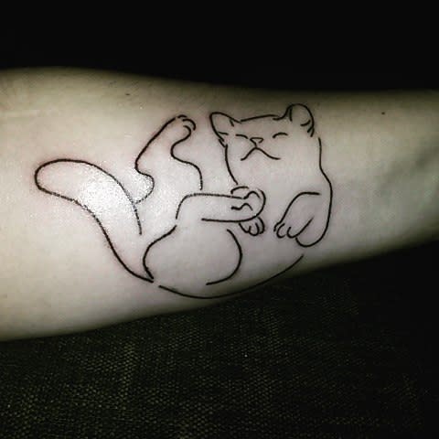 Minimalist line drawing tattoo of a sleeping cat elegantly etched on an arm