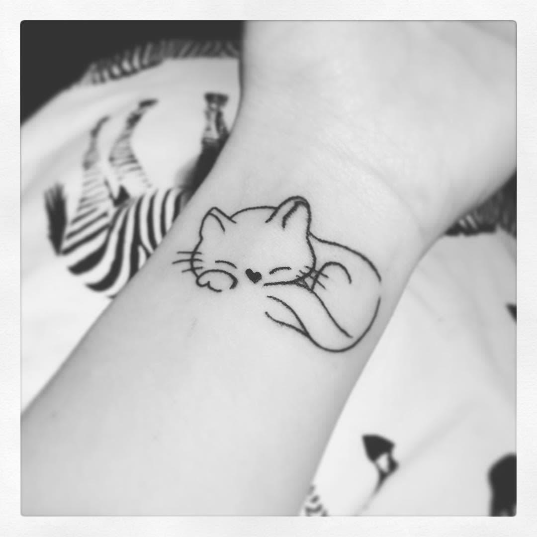 A simple line tattoo of a sleeping cat with a heart nose on a wrist