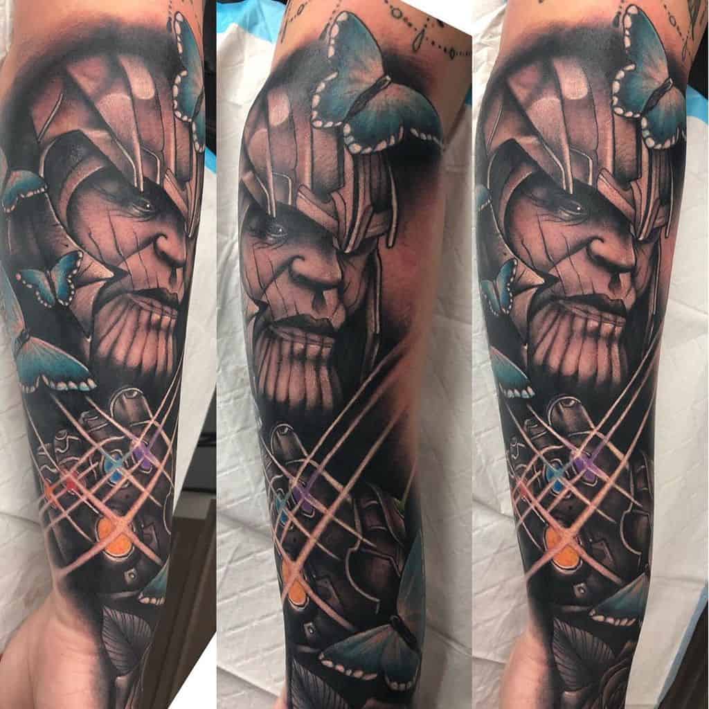 A detailed tattoo of Thanos with butterflies surrounding his head, featuring the Infinity Gauntlet with glowing stones and intricate shading