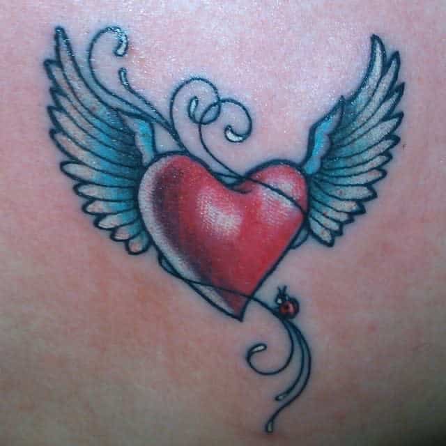 Tattoo of a vibrant red heart with expressive blue wings and a small ladybug resting beneath