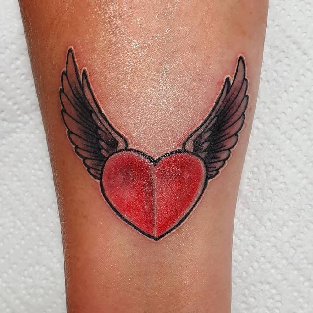 Tattoo of a vibrant red heart adorned with elegantly detailed black and gray wings on skin