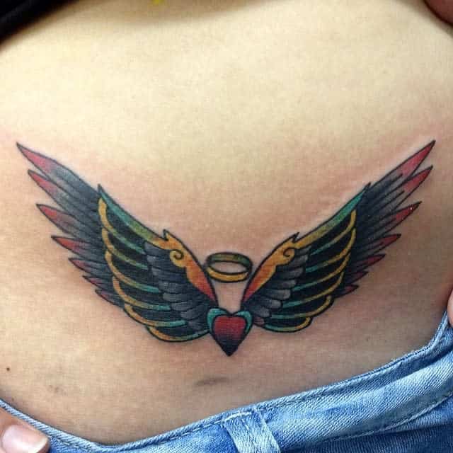A vibrant tattoo of wings envelops a heart with a halo, beautifully positioned on a person's lower back