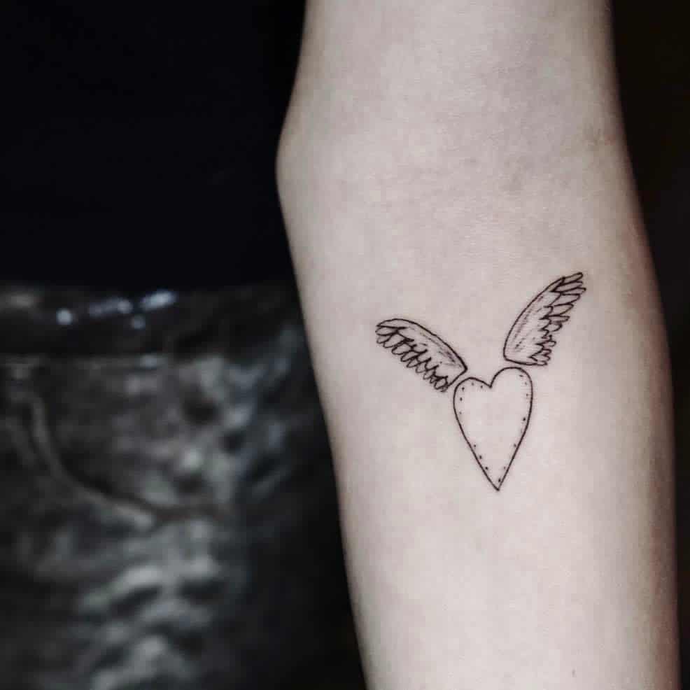 Tattoo of a heart adorned with wings on a person's forearm
