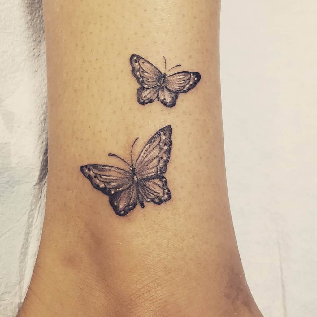Two realistic butterfly tattoos on a woman's ankle, one larger above the ankle and the other smaller above it