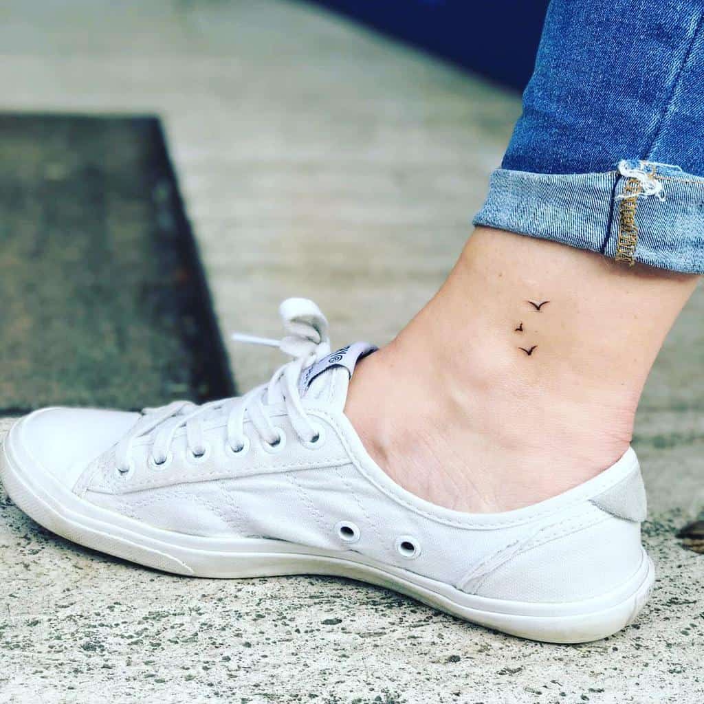 Minimalist ankle tattoo of three small birds in flight, symbolizing freedom and adventure, placed just above the foot for a subtle look