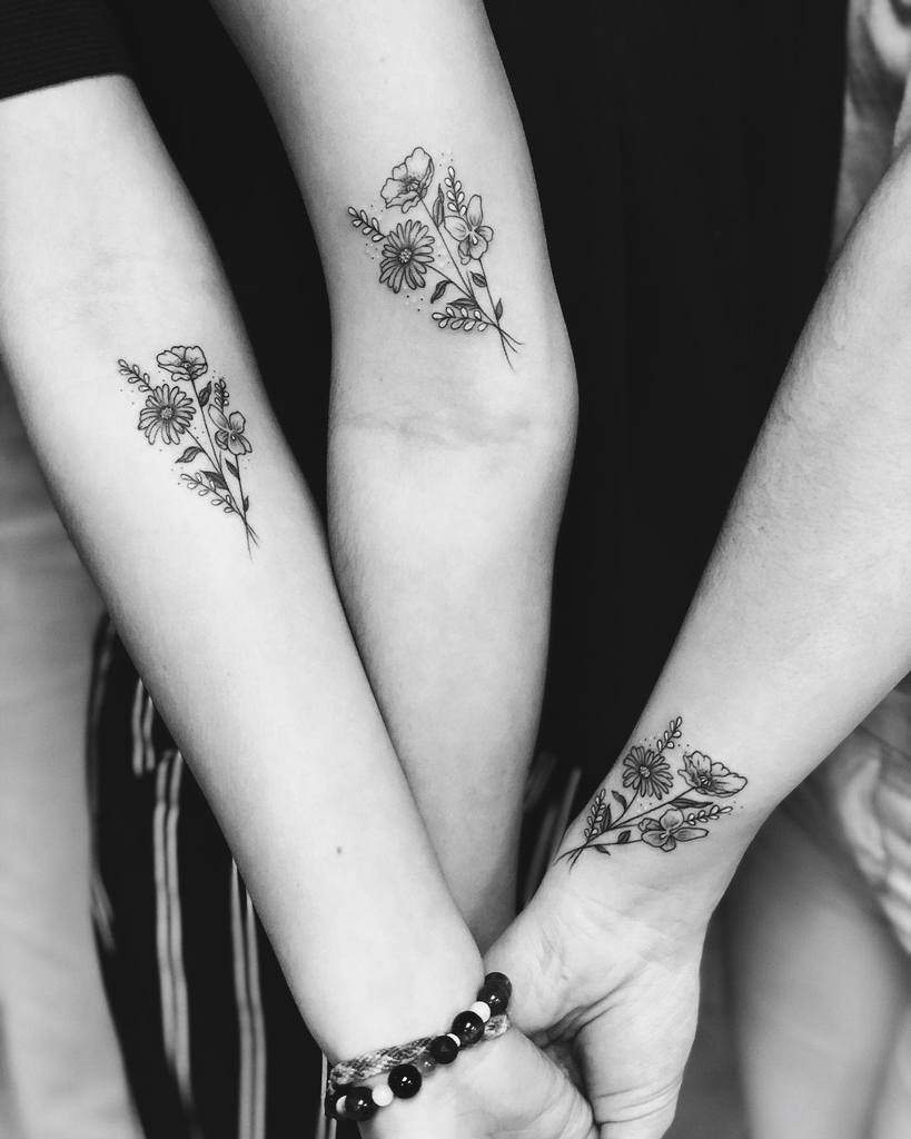 Line-art flower tattoos of delicate asters on three forearms joined hands