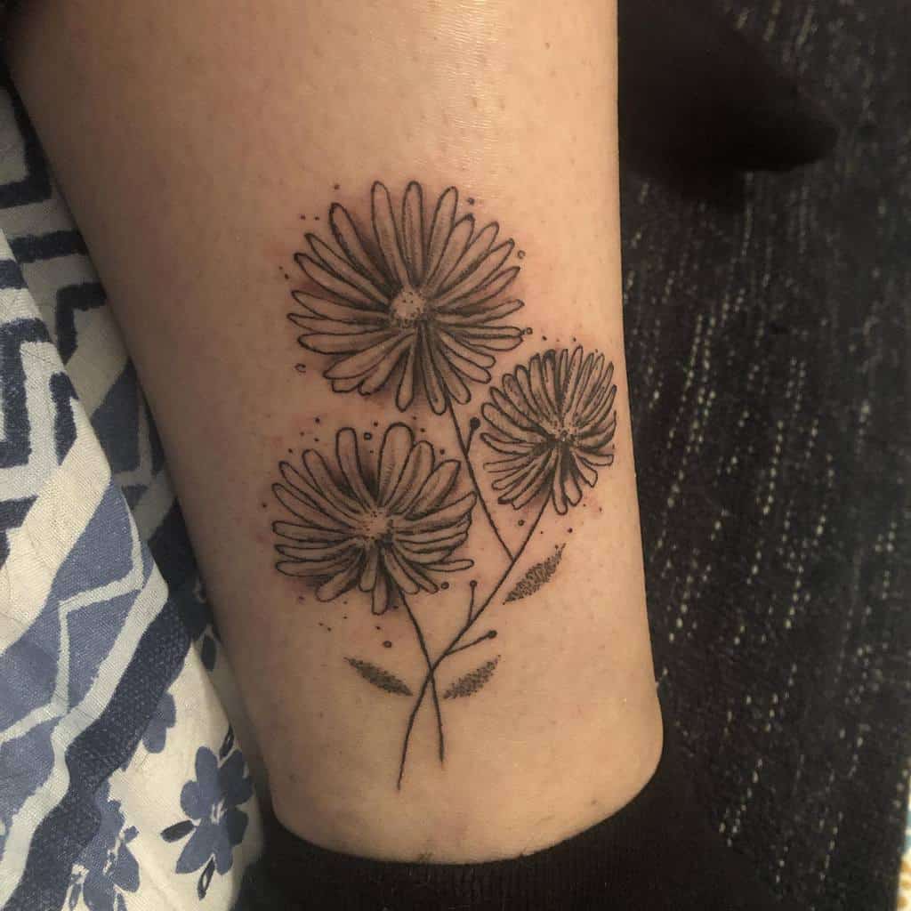 Tattoo of three daisies asters, with leaves and dots, on the inner forearm