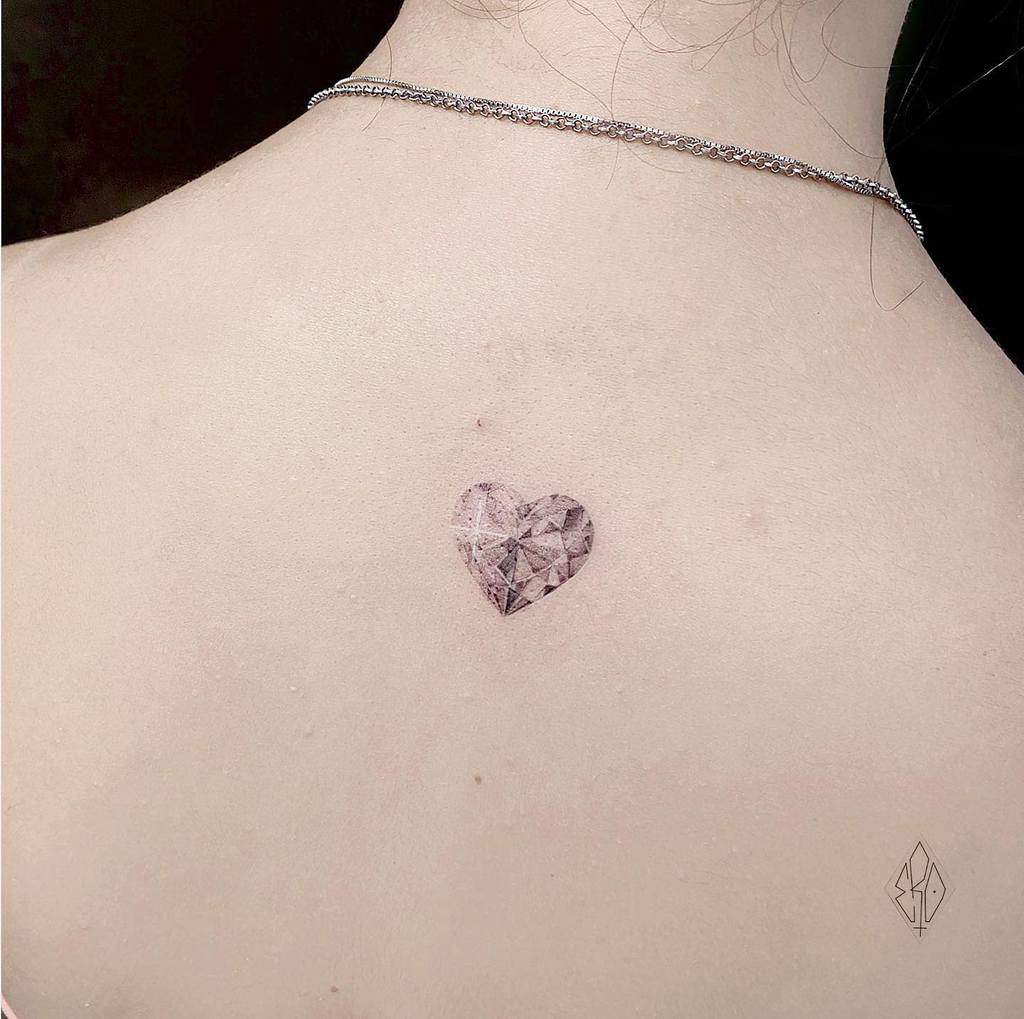 A small heart-shaped gemstone tattoo on a woman's upper back