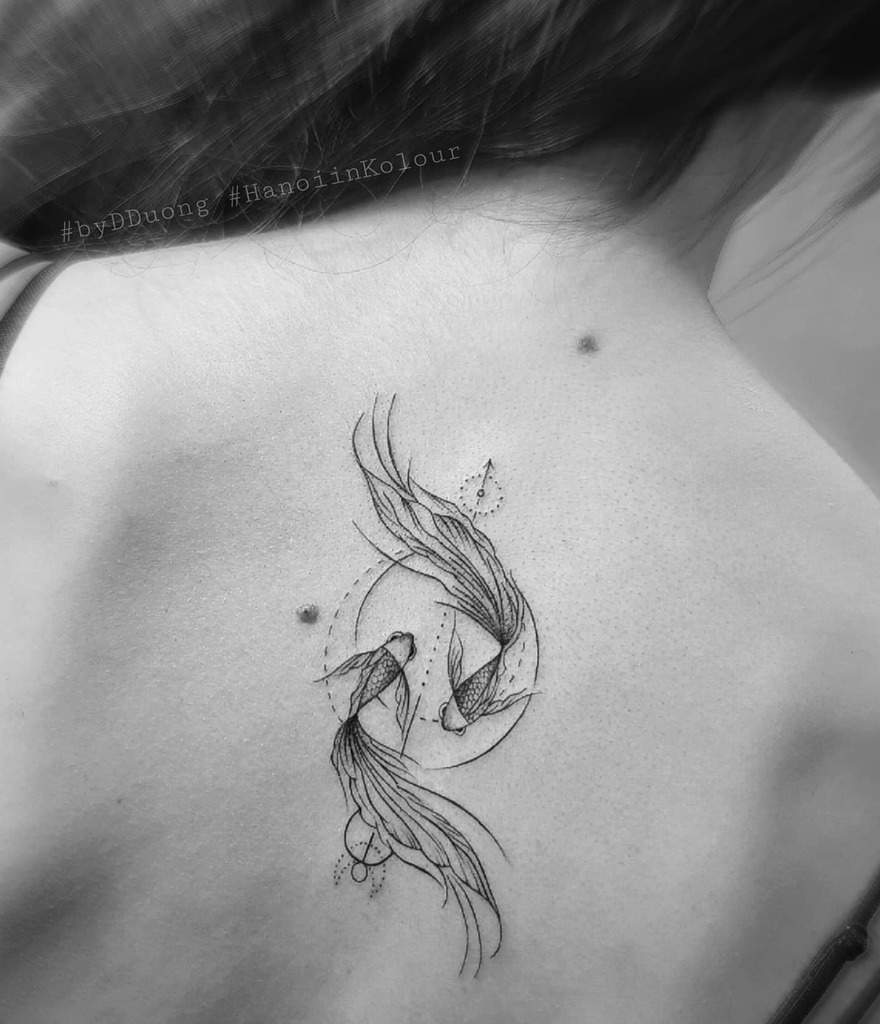 Black and white tattoo of two koi fish forming a circle on a woman's upper back