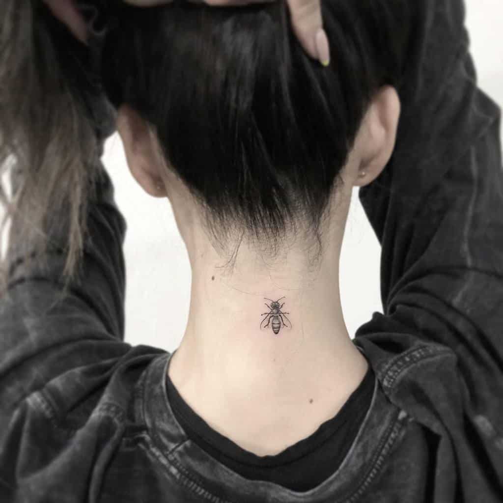Back of a person's neck with an ant tattoo, hair pulled up and wearing a dark shirt